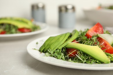 Photo of Delicious vegetable salad with avocado and microgreens served on light table, closeup