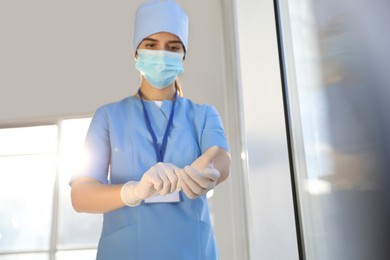 Photo of Doctor in protective mask and scrubs putting on medical gloves indoors. Space for text