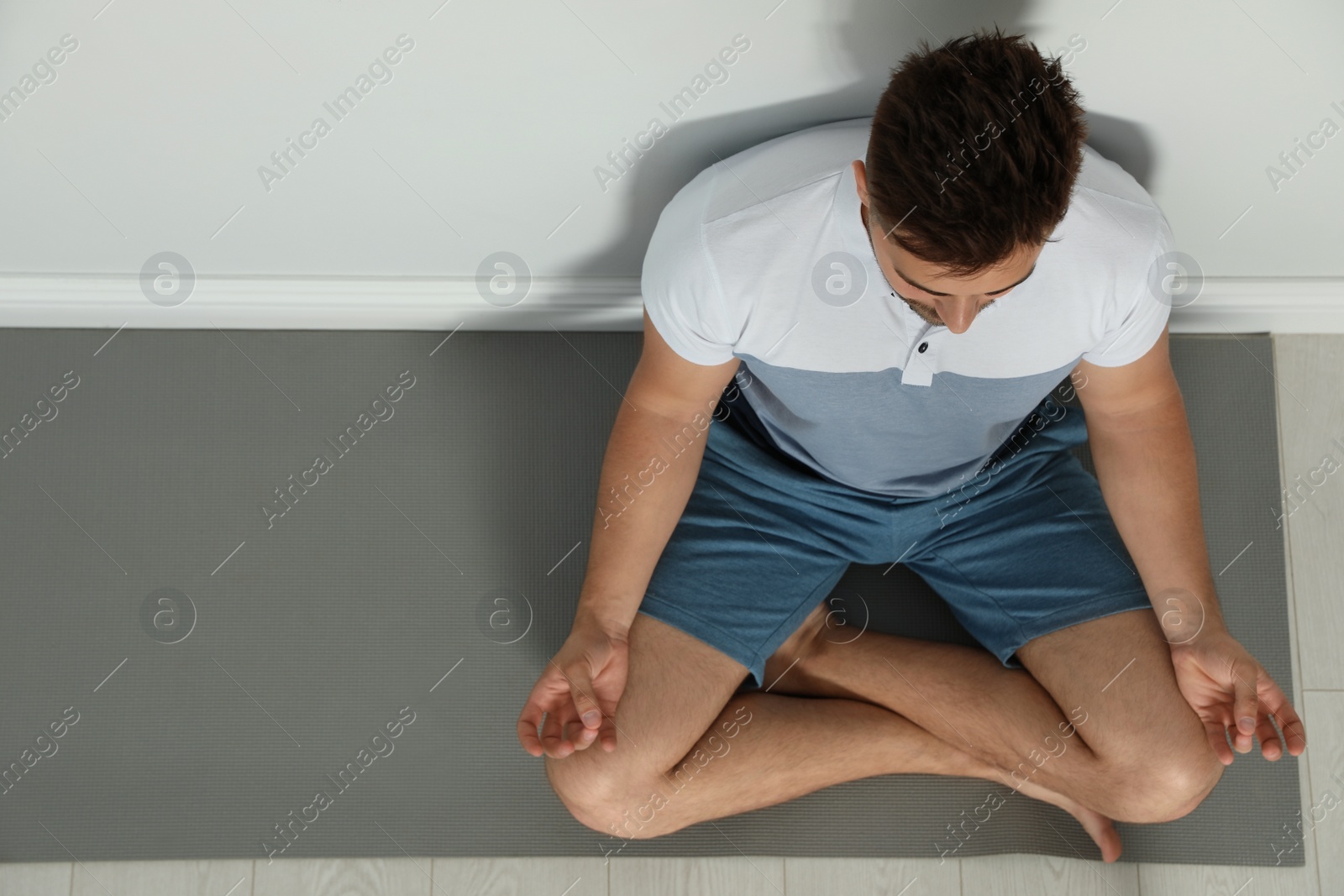 Photo of Young man practicing zen yoga near wall indoors, above view. Space for text