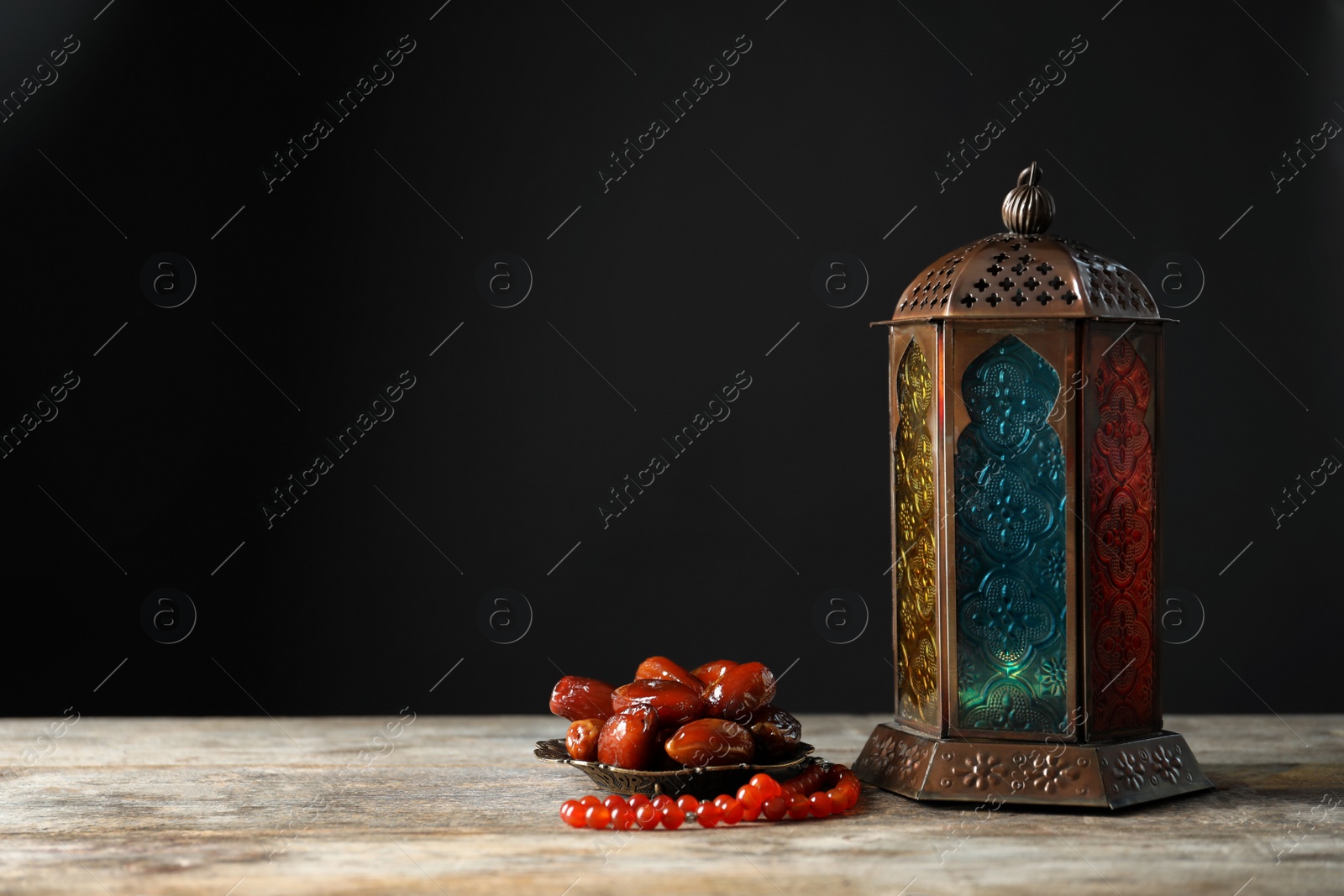 Photo of Muslim lamp, dates and misbaha on wooden table. Fanous as Ramadan symbol