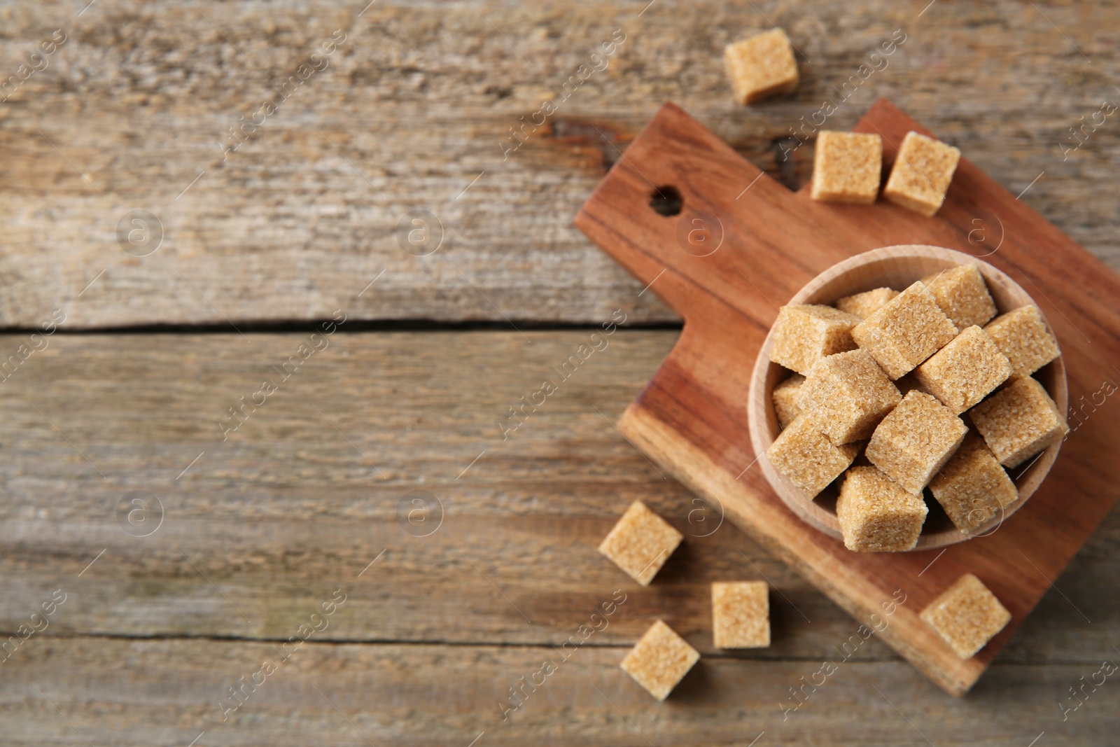 Photo of Bowl with brown sugar cubes on wooden table, flat lay. Space for text