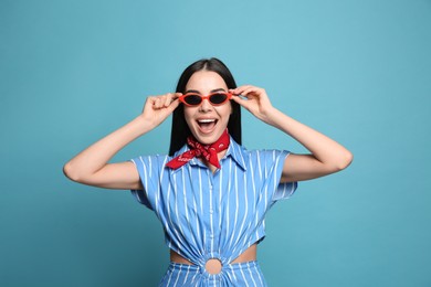 Photo of Fashionable young woman in stylish outfit with bandana on light blue background