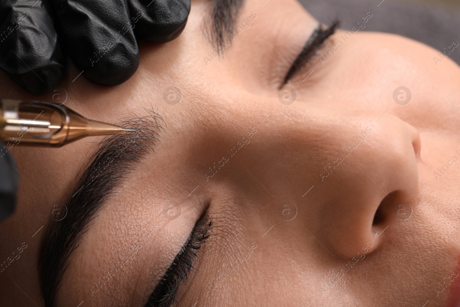 Photo of Young woman undergoing procedure of permanent eyebrow makeup in tattoo salon, closeup