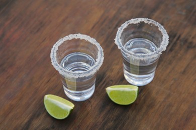 Photo of Mexican tequila shots with lime slices and salt on wooden table, above view