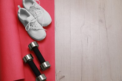 Photo of Dumbbells, sneakers and mat on wooden floor, above view. Space for text