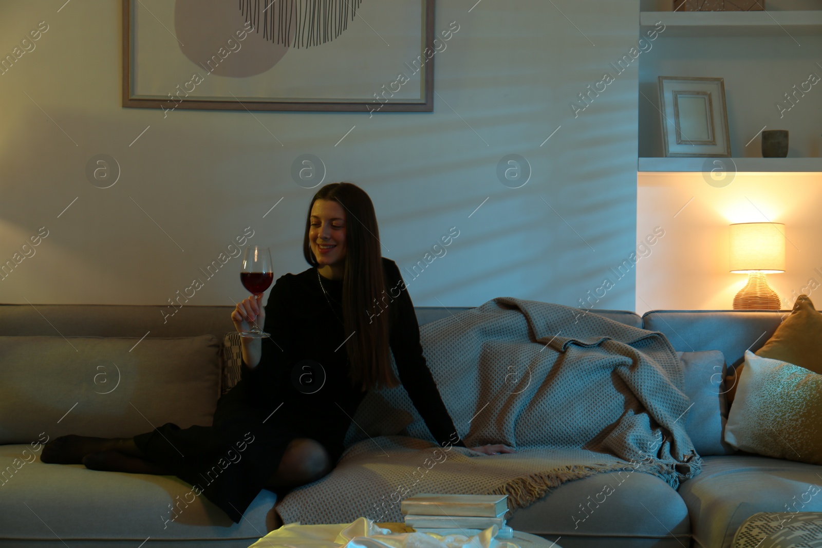 Photo of Woman with glass of wine resting on couch in room at night