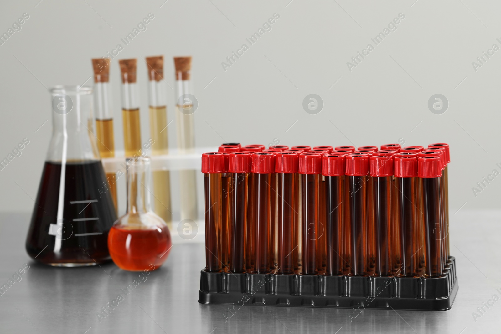 Photo of Different laboratory glassware with brown liquids on table against light background