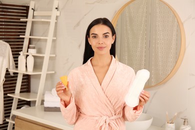 Photo of Young woman with menstrual cup and pad in bathroom