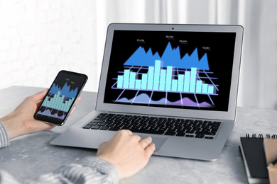 Image of Broker working with laptop and mobile phone at table, closeup. Forex trading