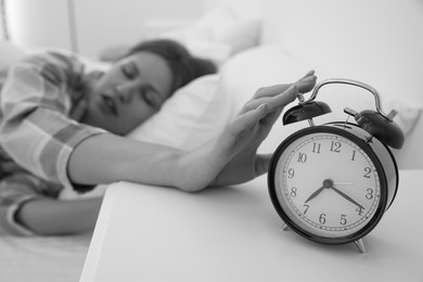 Image of Sleepy young woman turning off alarm clock at home in morning, selective focus. Black and white photography