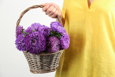 Photo of Woman with bouquet of beautiful asters on light background, closeup. Autumn flowers