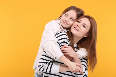 Portrait of happy mother and her cute daughter on orange background. Space for text