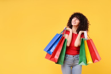 Happy young woman with shopping bags on yellow background. Space for text