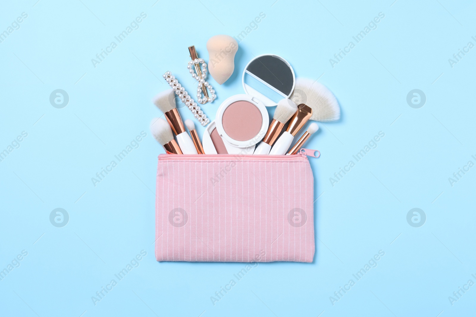 Photo of Cosmetic bag with makeup products and beauty accessories on light blue background, flat lay