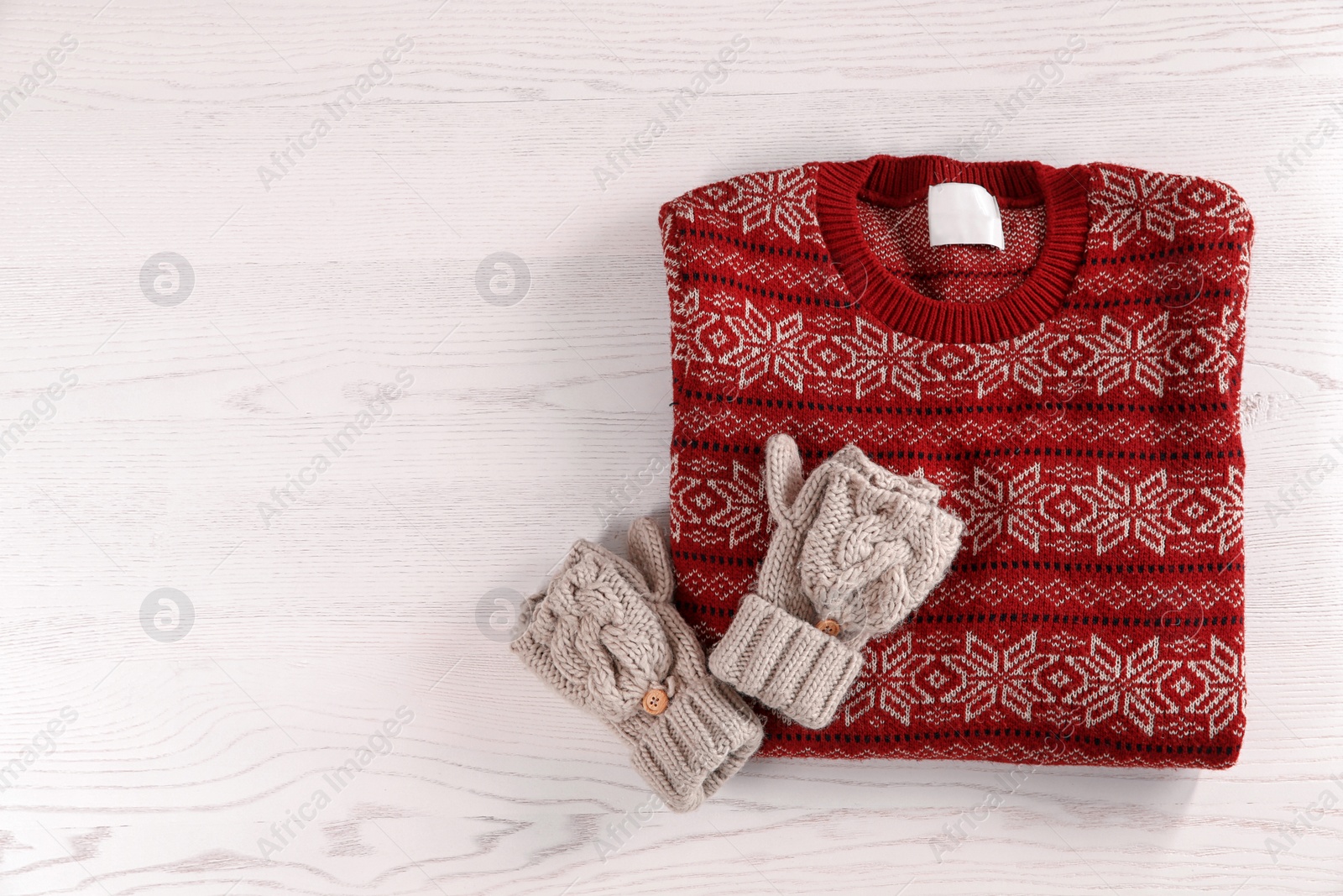 Photo of Knitted mittens and Christmas sweater with pattern on wooden background, top view. Space for text