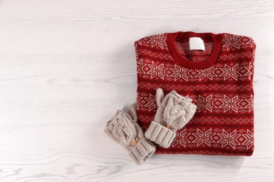 Photo of Knitted mittens and Christmas sweater with pattern on wooden background, top view. Space for text