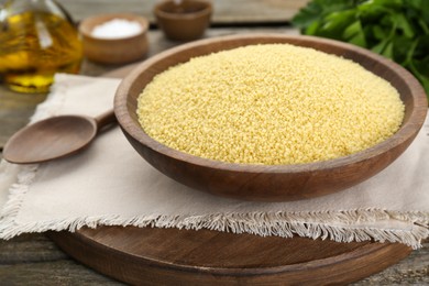 Bowl of raw couscous on wooden table, closeup