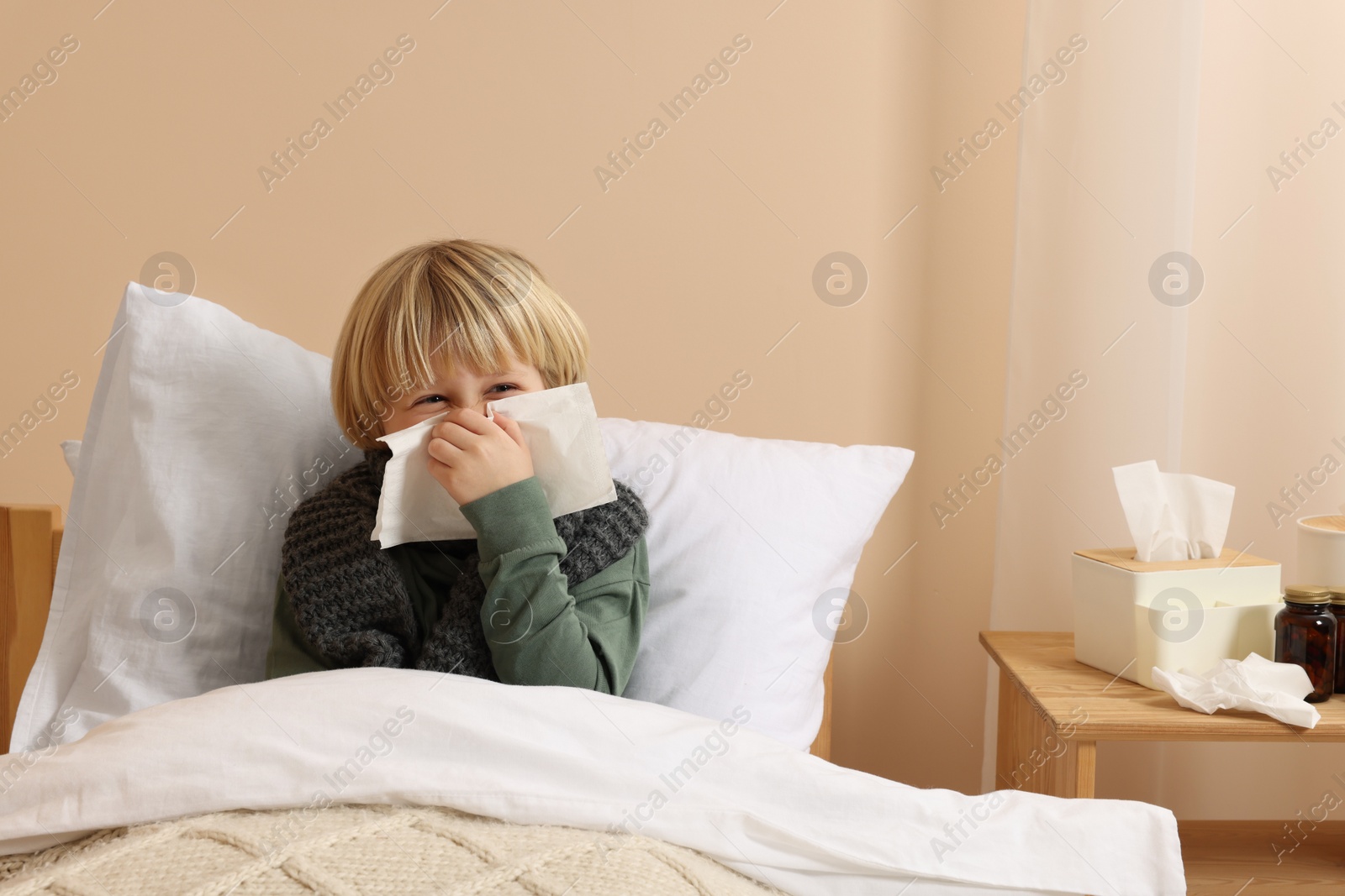 Photo of Boy blowing nose in tissue in bed at home. Cold symptoms