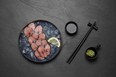 Photo of Raw mackerel slices, ice cubes and lemon served with vasabi and soy sauce on grey table, flat lay. Fish delicacy