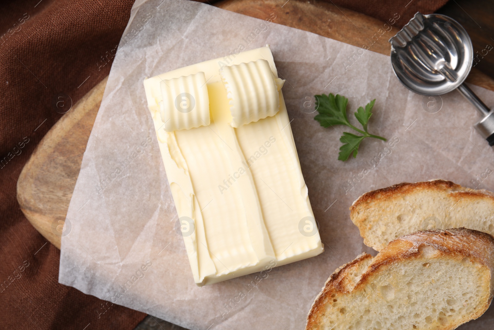 Photo of Tasty butter, slices of bread and spoon on wooden table, top view