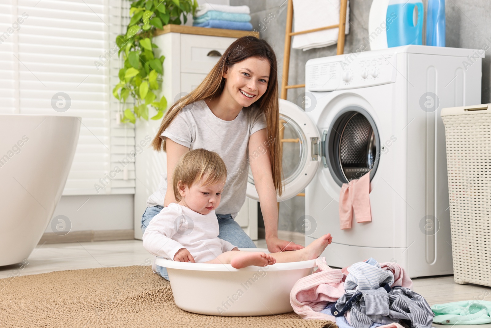 Photo of Happy mother with her daughter having fun while washing baby clothes in bathroom