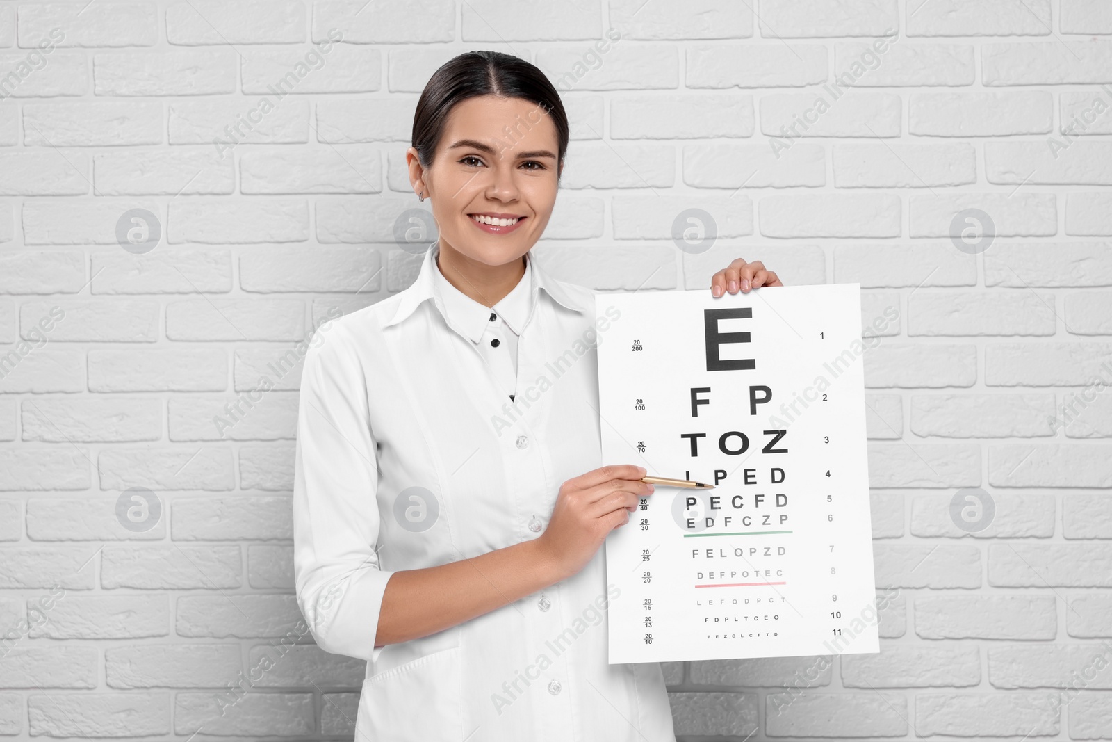 Photo of Ophthalmologist pointing at vision test chart near white brick wall