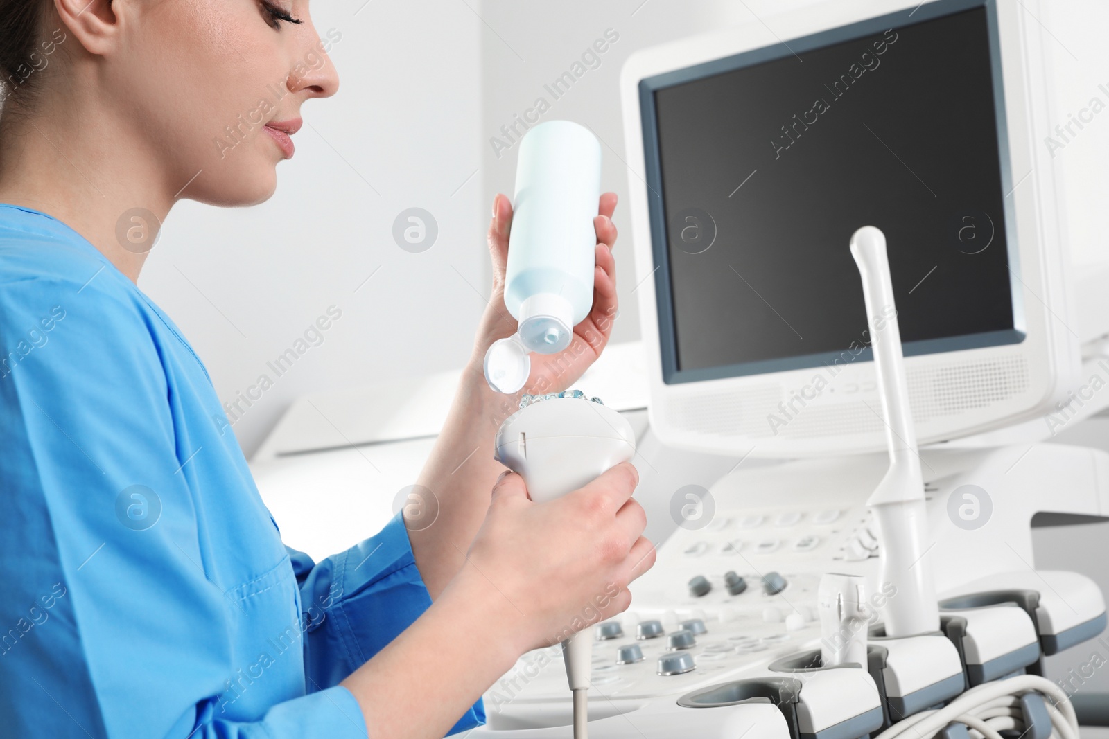 Photo of Sonographer covering ultrasound machine probe with gel in clinic, closeup