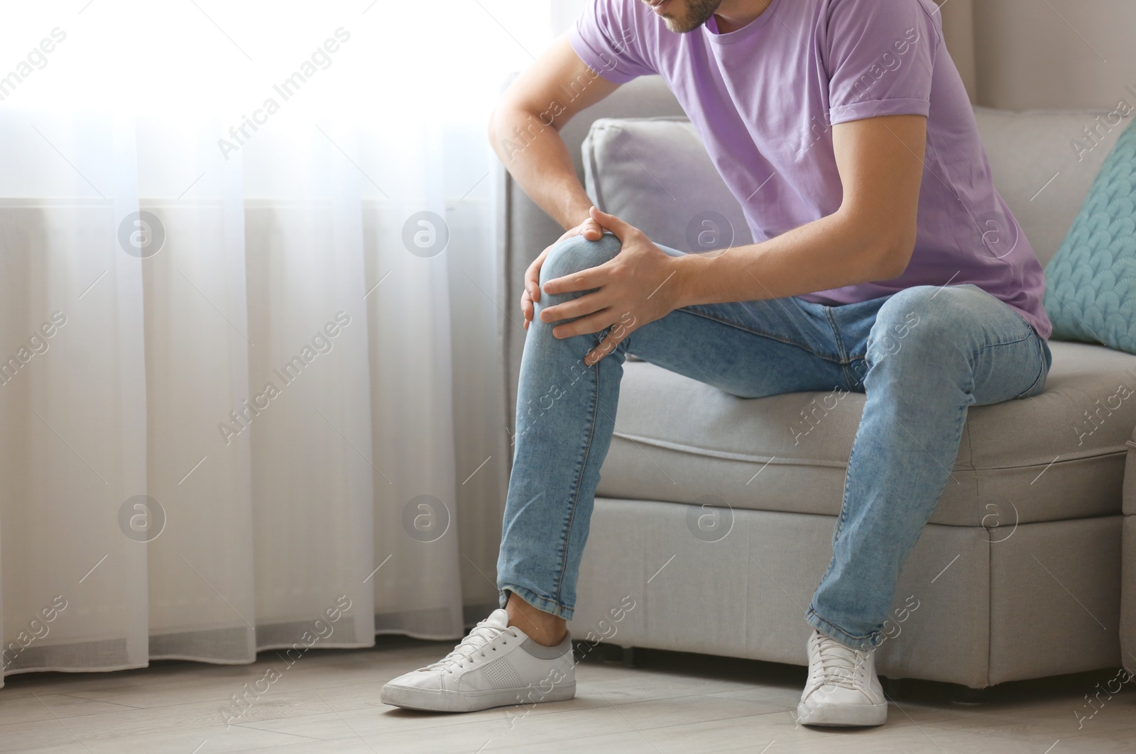 Photo of Young man suffering from knee pain at home