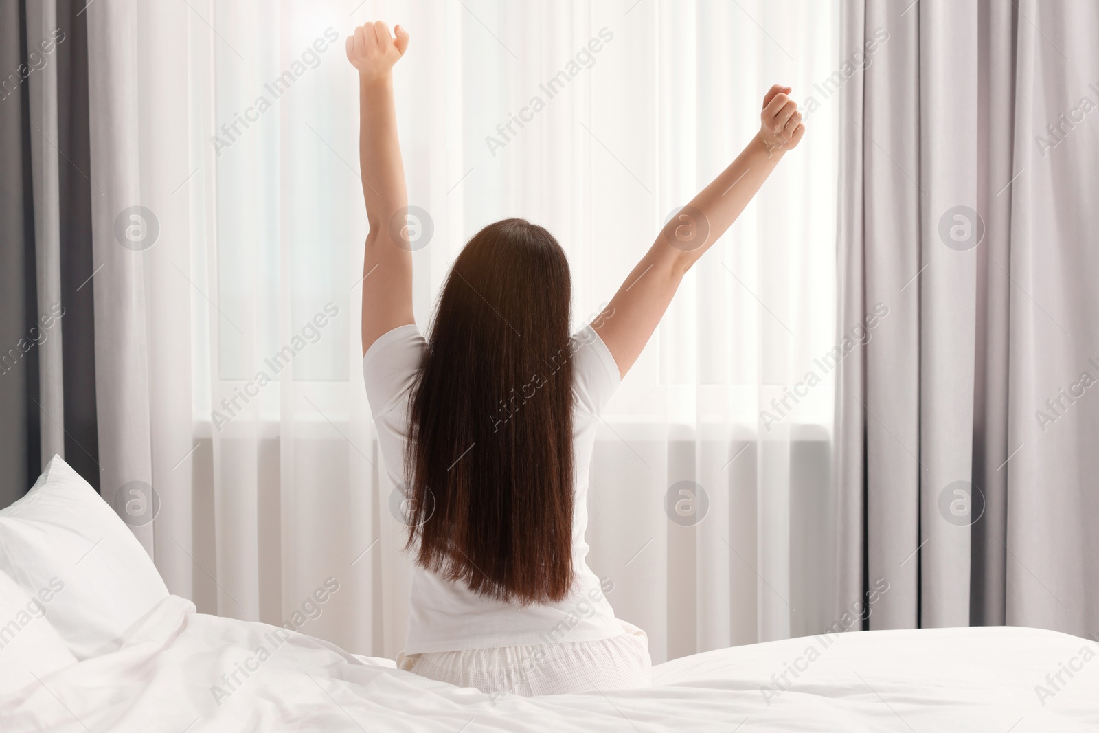 Photo of Woman stretching on bed at home, back view. Lazy morning