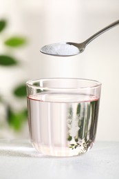 Adding baking soda into glass of water at white table against blurred background