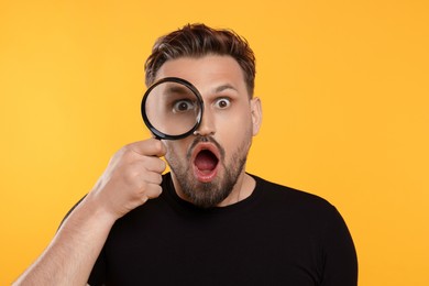 Photo of Emotional man looking through magnifier on yellow background
