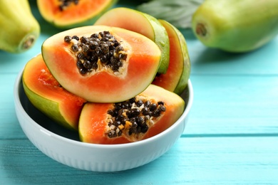 Photo of Cut fresh ripe papaya in bowl on turquoise wooden table, closeup