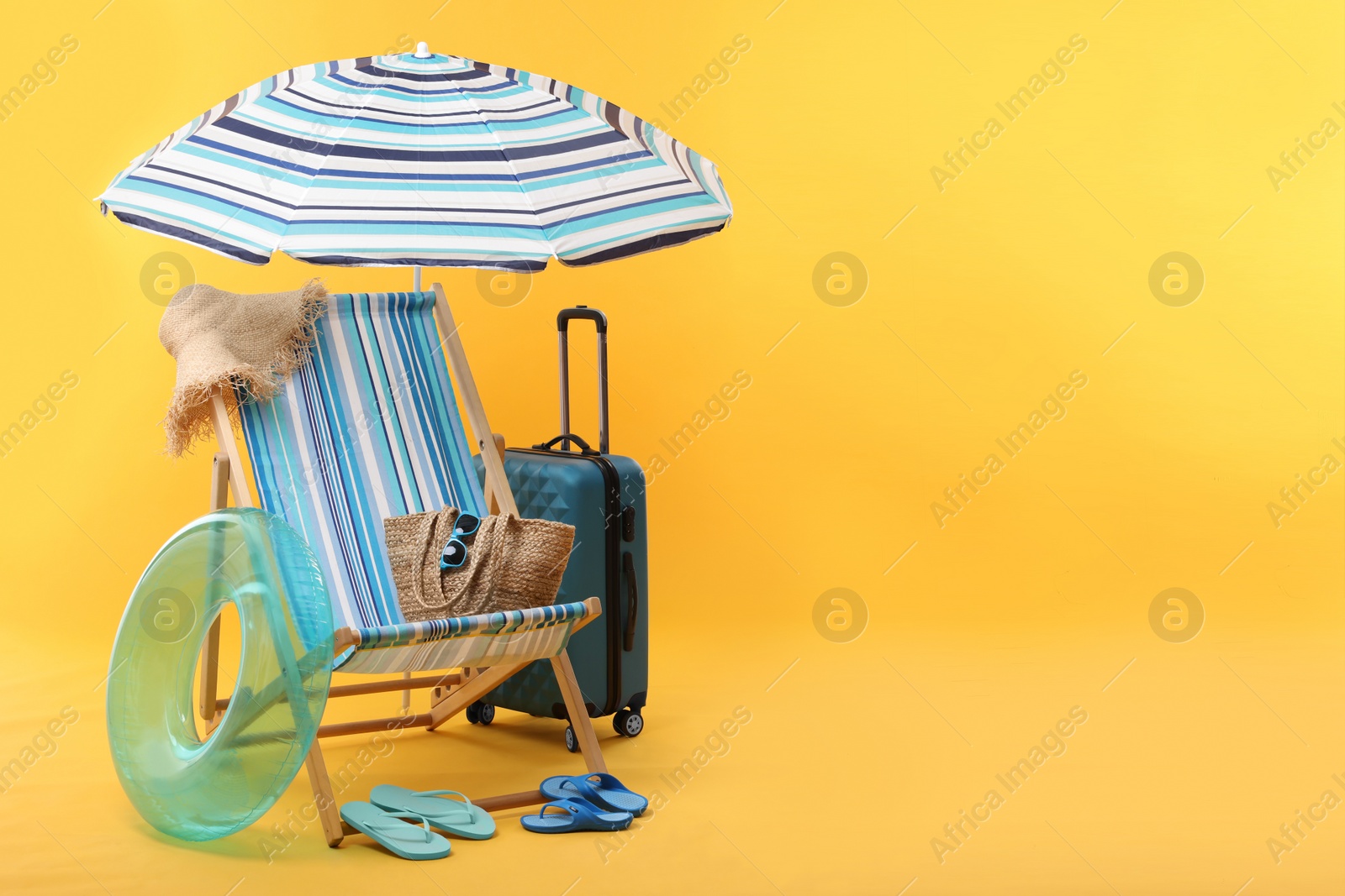 Deck chair, umbrella, suitcase and beach accessories on yellow background, space for text. Summer vacation Photo of Deck chair, umbrella, suitcase and beach accessories on yellow background, space for text. Summer vacation