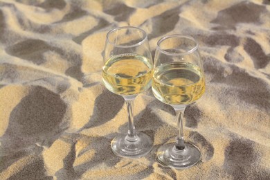 Photo of Glasses of tasty wine on sand, space for text