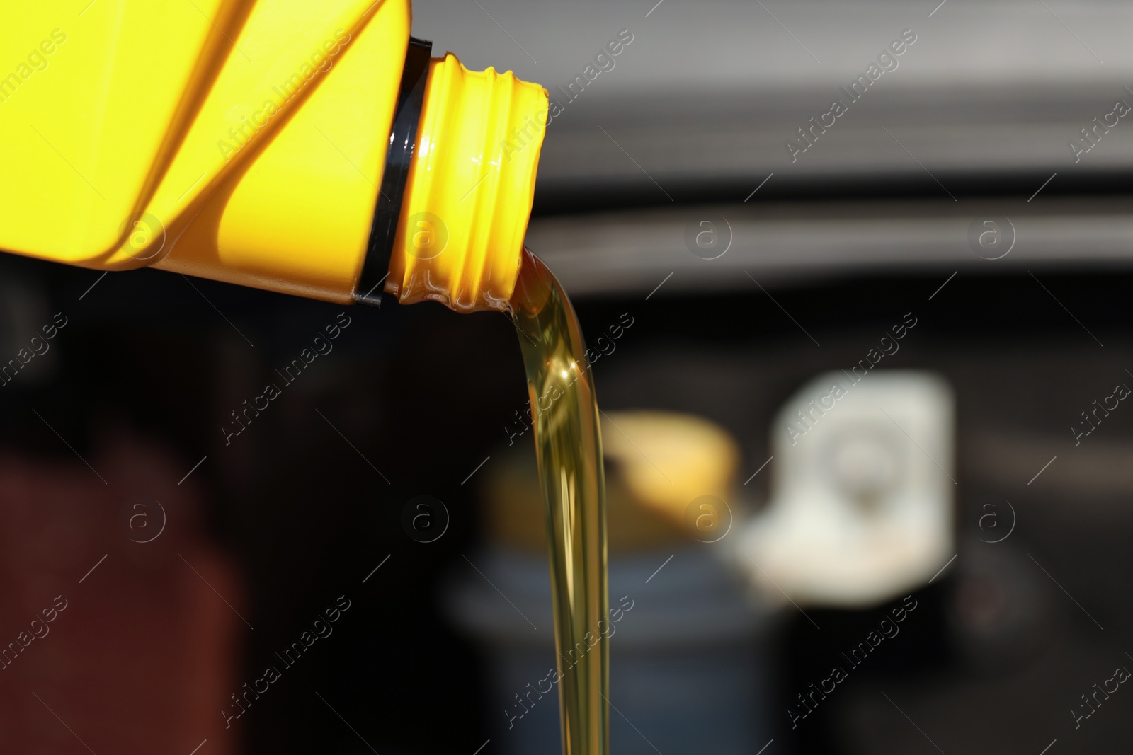 Photo of Pouring motor oil from yellow container against blurred background, closeup. Space for text