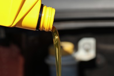 Photo of Pouring motor oil from yellow container against blurred background, closeup. Space for text