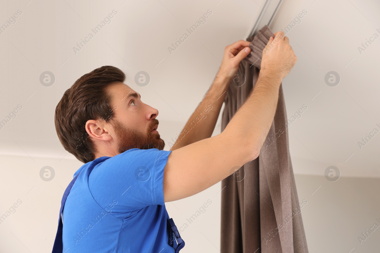 Photo of Worker in uniform hanging window curtain indoors