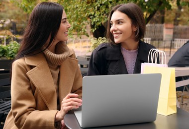 Special Promotion. Happy young women with shopping bags using laptop in outdoor cafe