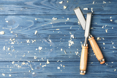 Modern chisels on blue wooden background, flat lay with space for text. Carpenter's tools