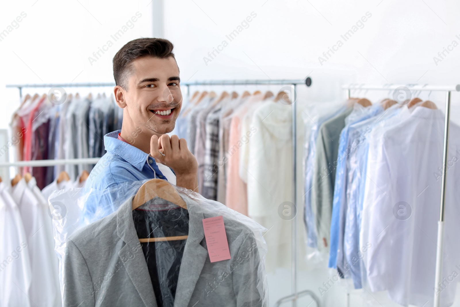 Photo of Young man holding hanger with jacket in plastic bag at dry-cleaner's