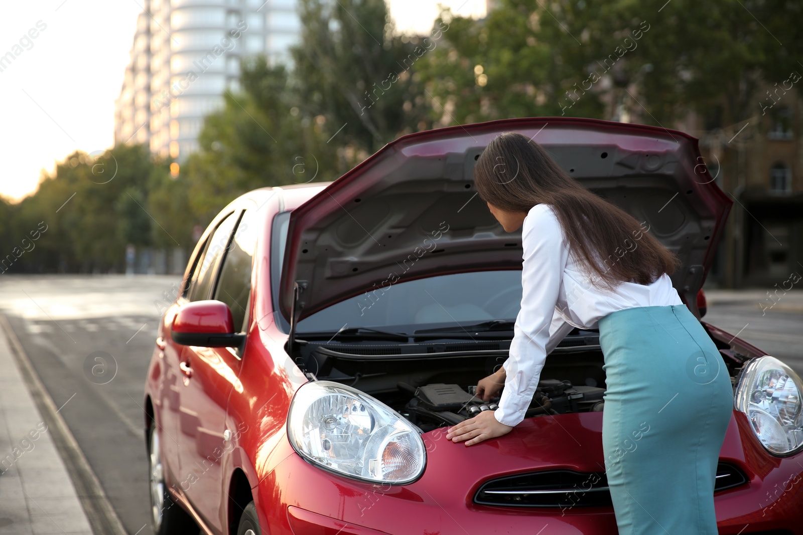 Photo of Young woman fixing broken car on city street