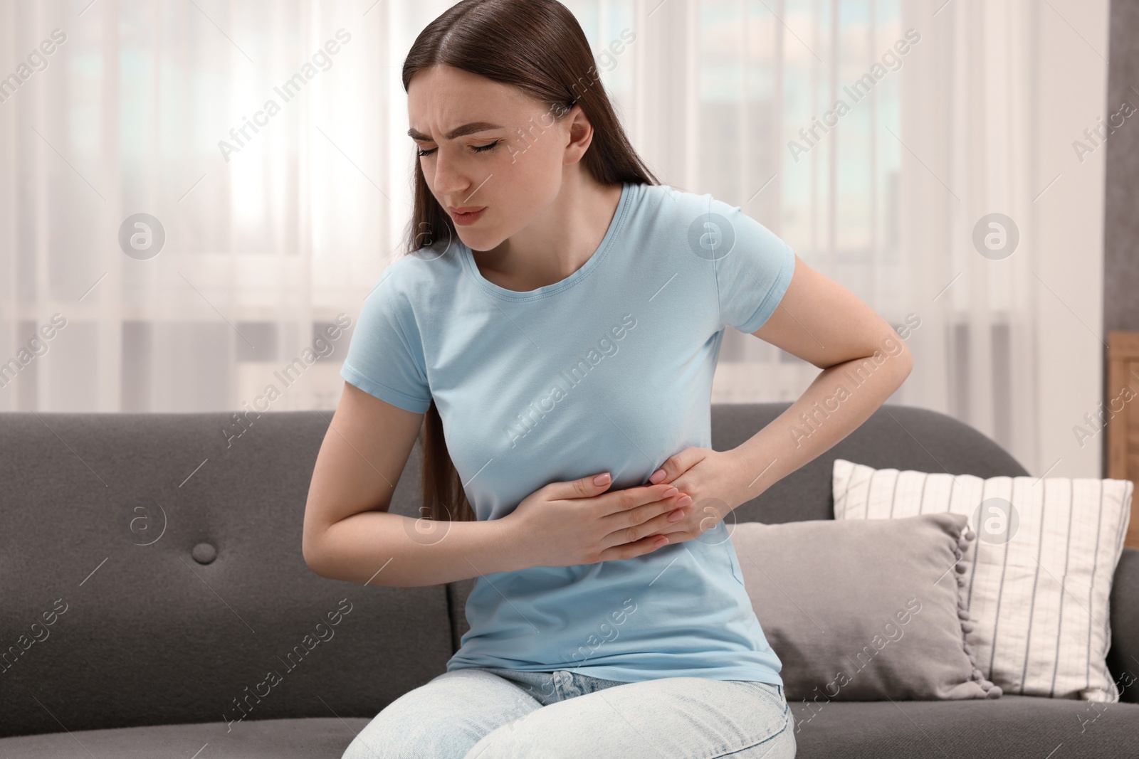 Photo of Woman suffering from stomach pain on sofa indoors