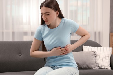 Woman suffering from stomach pain on sofa indoors