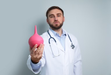 Photo of Doctor holding rubber enema against grey background, focus on hand