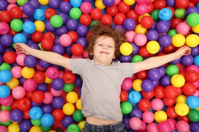 Photo of Happy little boy lying on many colorful balls, top view
