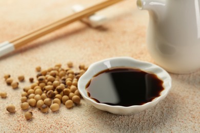 Soy sauce in bowl and beans on beige textured table, closeup