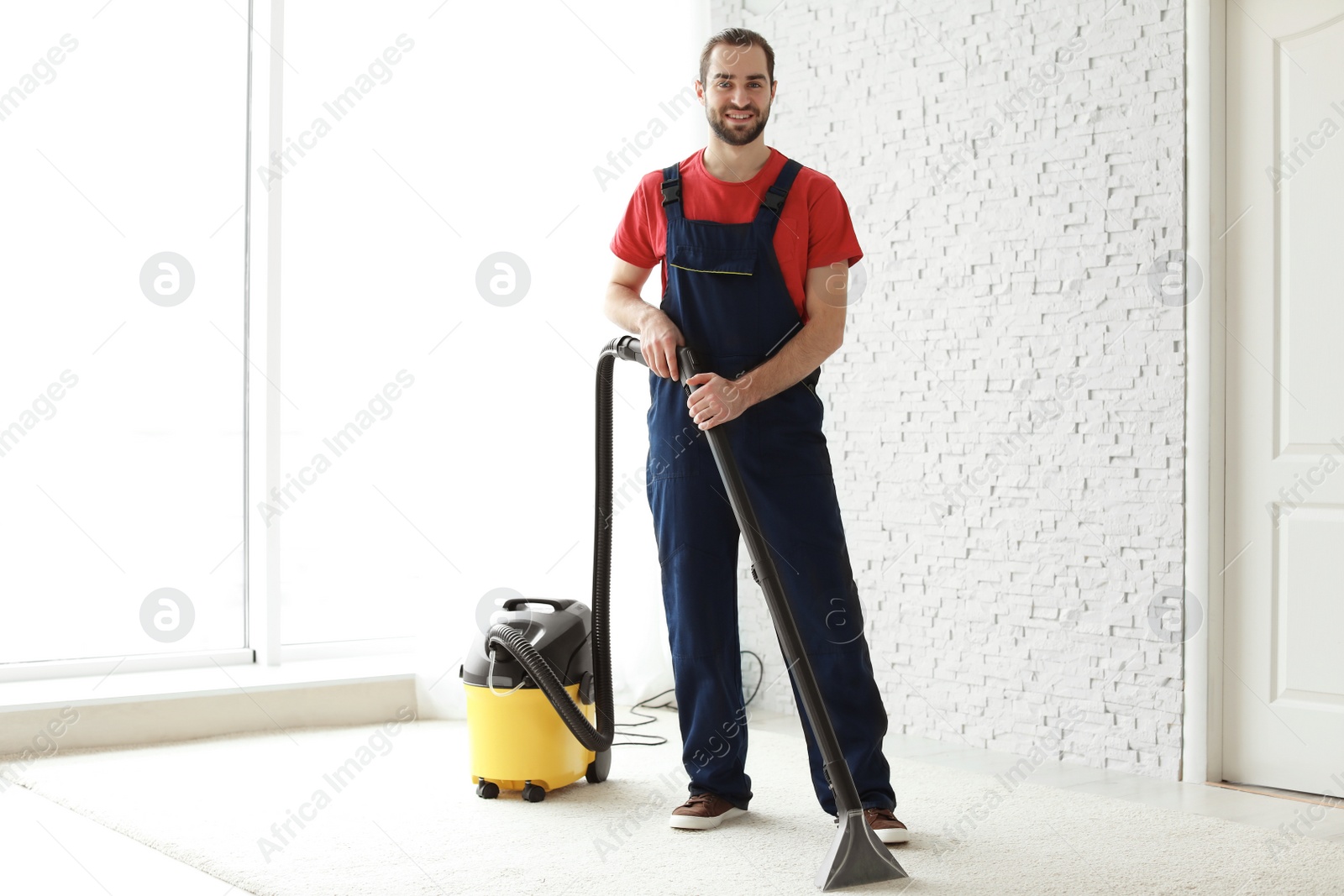 Photo of Male worker cleaning carpet with vacuum indoors