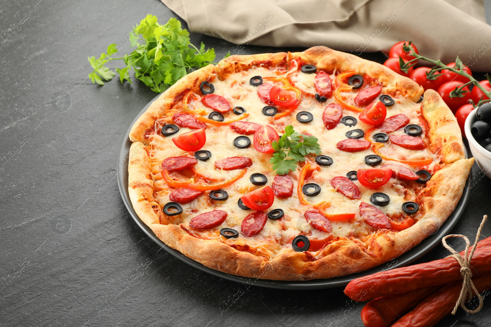 Photo of Tasty pizza with dry smoked sausages, olives, tomatoes, pepper and parsley on grey table