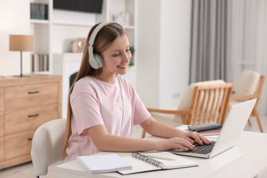 Photo of Online learning. Teenage girl in headphones typing on laptop at table