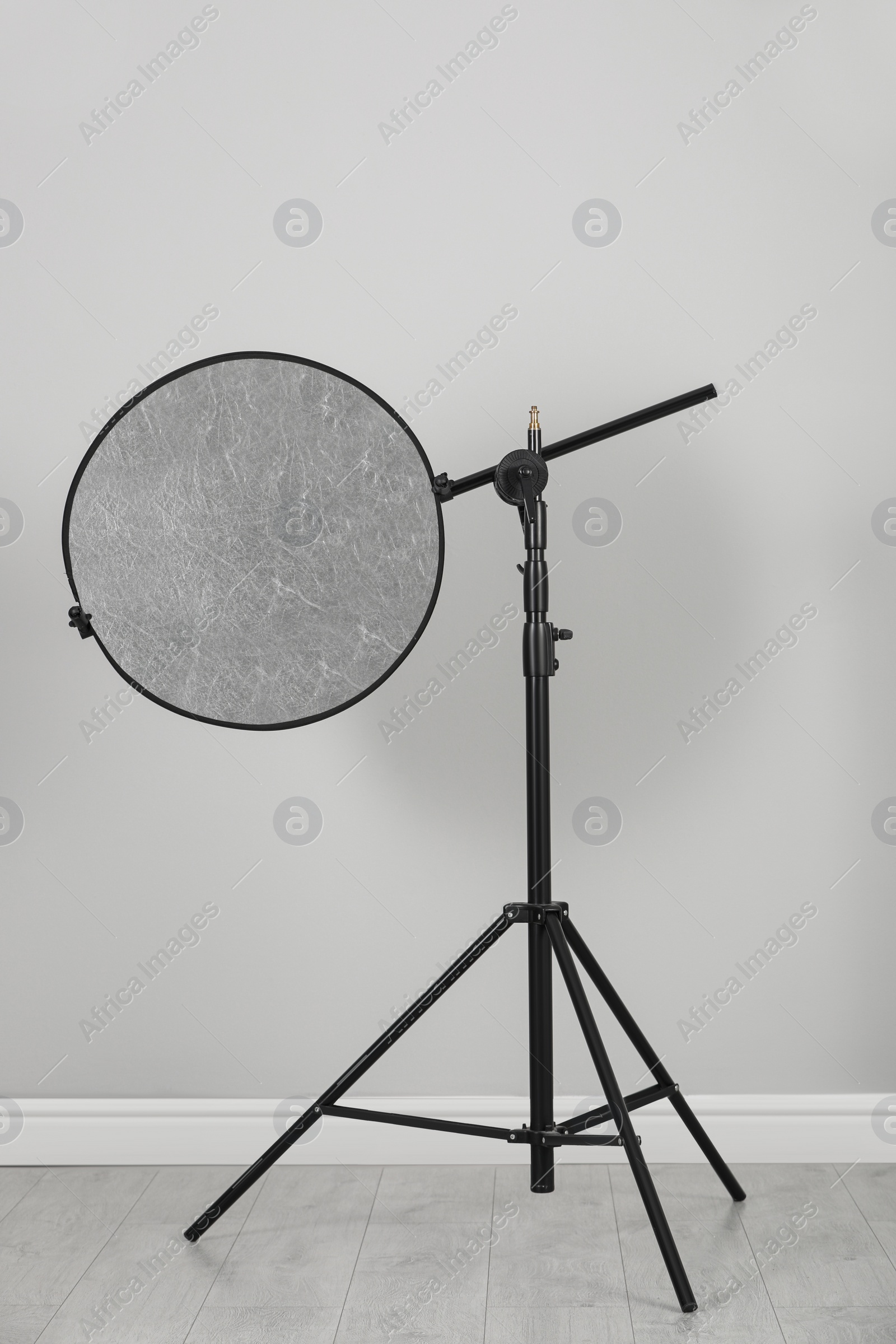 Photo of Studio reflector on tripod near grey wall indoors. Professional photographer's equipment